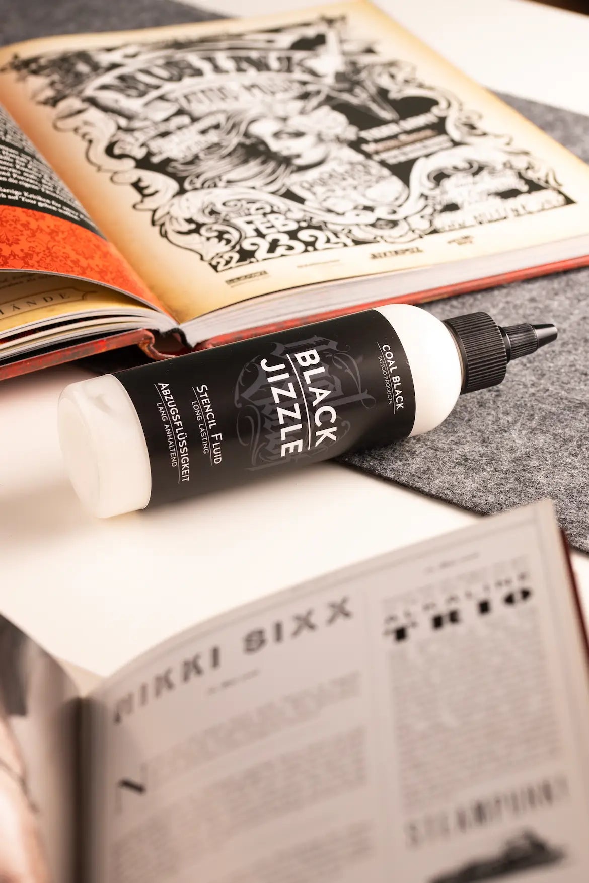 A sleek black and white bottle of coal black black jizzle stencil fluid with a fine-tipped nozzle for precise ink application