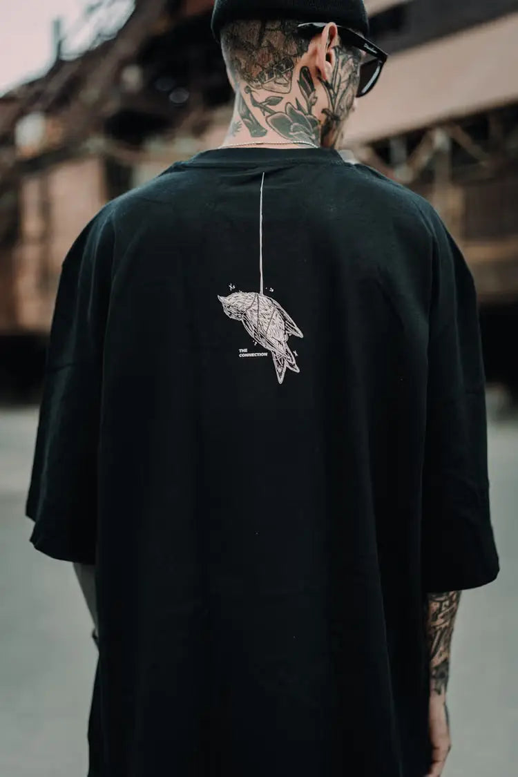 Black oversized tee unisex with white line art bird graphic on the back from wolfpack connection collection wears size