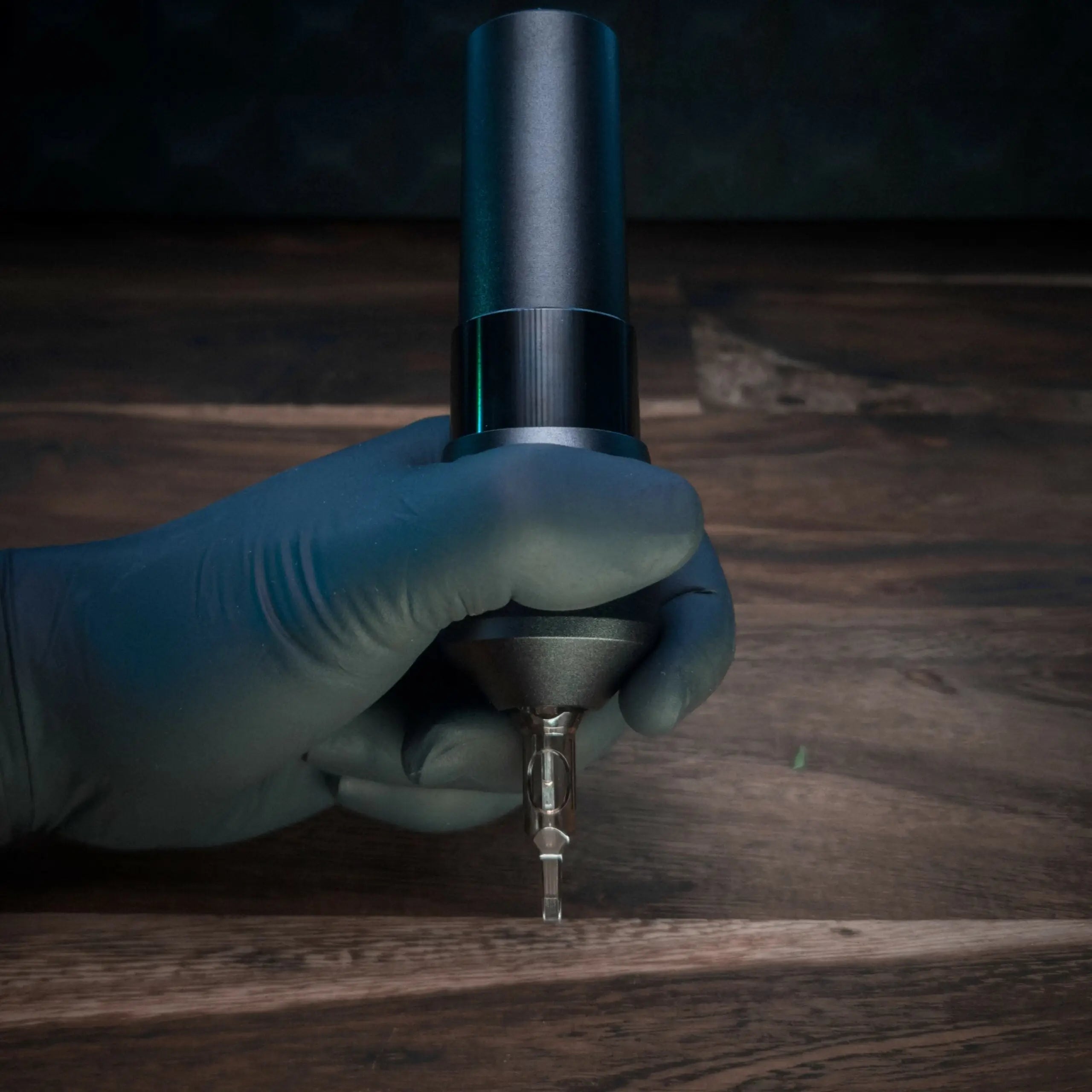 Schwarze und silberne ACUS M1 Grip Plus Tattoo-Maschine mit metallischer Nadel-TIP, gehalten in einer behandschuhten Hand für präzises Tätowieren