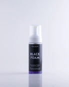 COAL BLACK schwarzer Reinigungsschaum in einer eleganten transparenten Flasche mit weißer Pumpe und violetter Flüssigkeit im Inneren