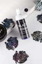 Eine elegante, durchscheinende violette Flasche mit beruhigendem und entspannendem Schaum in COAL BLACK, mit weißer Sprühdüse und schwarzem Etikett