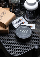 Black circular container of coal black black lube vegan ointment tattoo product for skin care and lubrication
