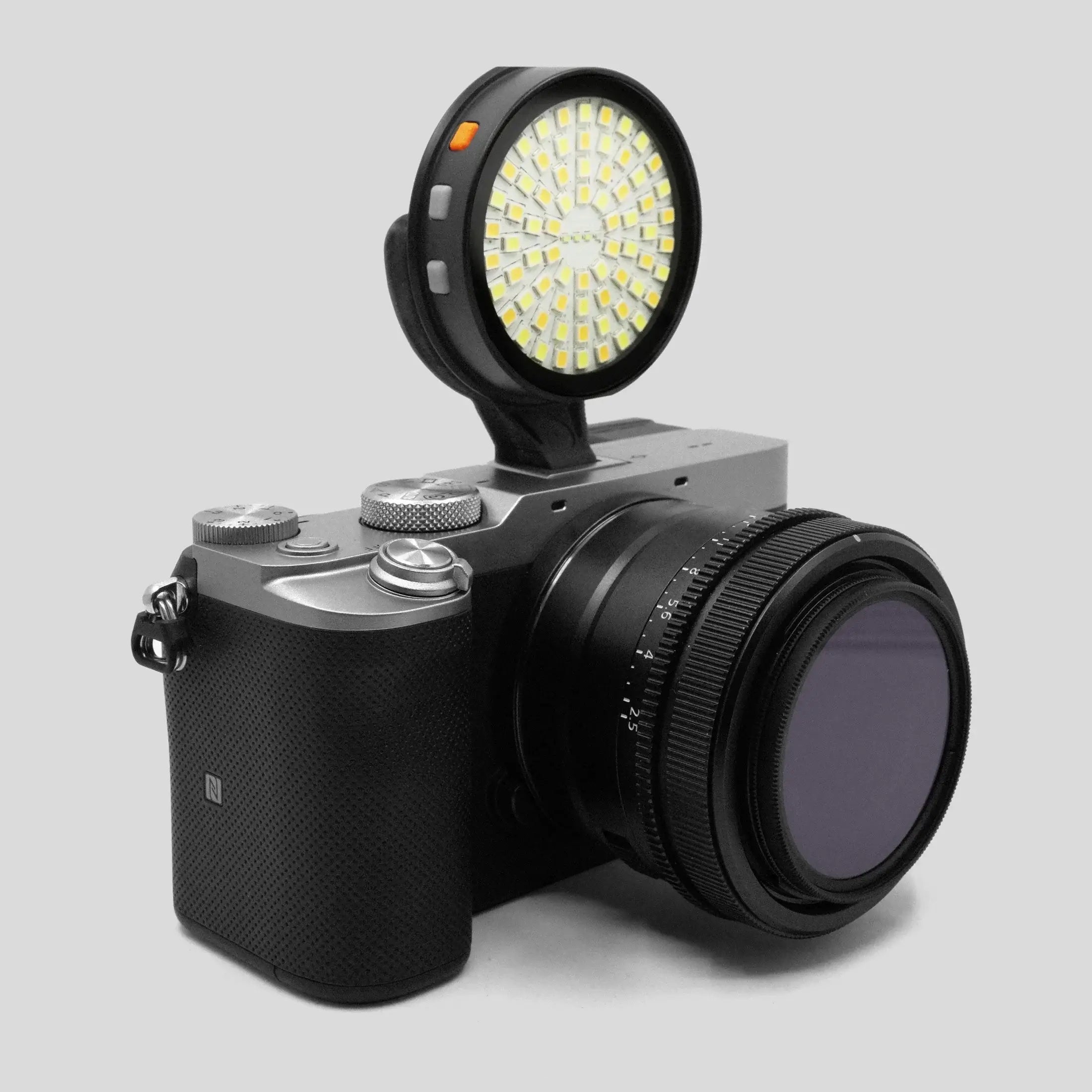 GOAT-Lichtstütze schwarze runde LED-Kameraleuchte mit gelben LEDs und orangefarbenem Einschaltknopf auf einer silbernen spiegellosen Kamera montiert