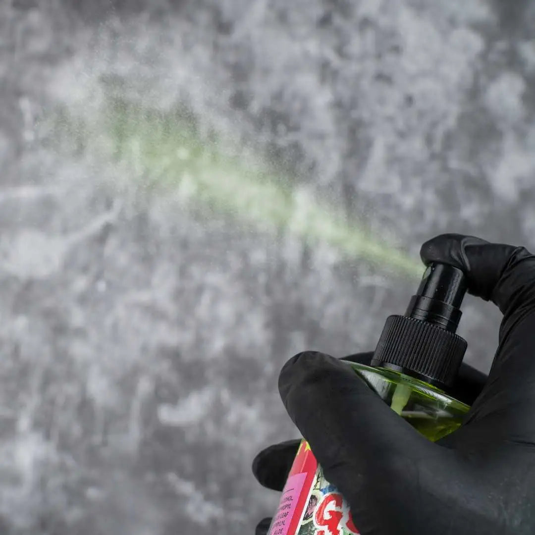 Eine Hand in schwarzen Handschuhen hält eine grüne good hand-Radierersprühflasche, die einen feinen Nebel hellgrüner Flüssigkeit versprüht