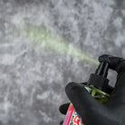 Eine Hand in schwarzen Handschuhen hält eine grüne good hand-Radierersprühflasche, die einen feinen Nebel hellgrüner Flüssigkeit versprüht