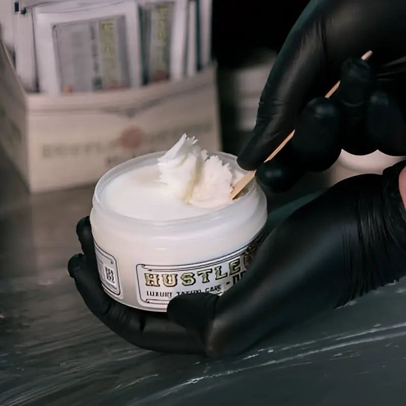 White jar of hustle butter deluxe luxury organic talcum cake with label and creamy white contents scooped by wooden stick