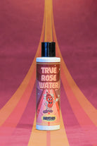 A vibrant pink and orange bottle of Kosmos true rose water with a black cap and a cartoon character design