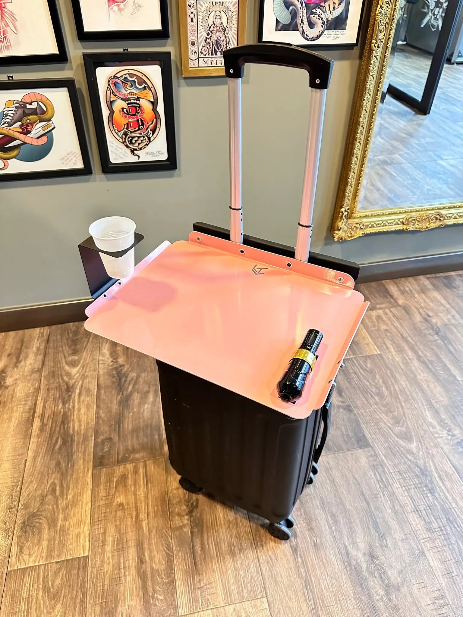 Rosa Kunststoff-Reisetablett von Lt Tattoo, befestigt an einem schwarzen Rollkoffer mit ausziehbarem Griff für einfache Nutzung auf Reisen