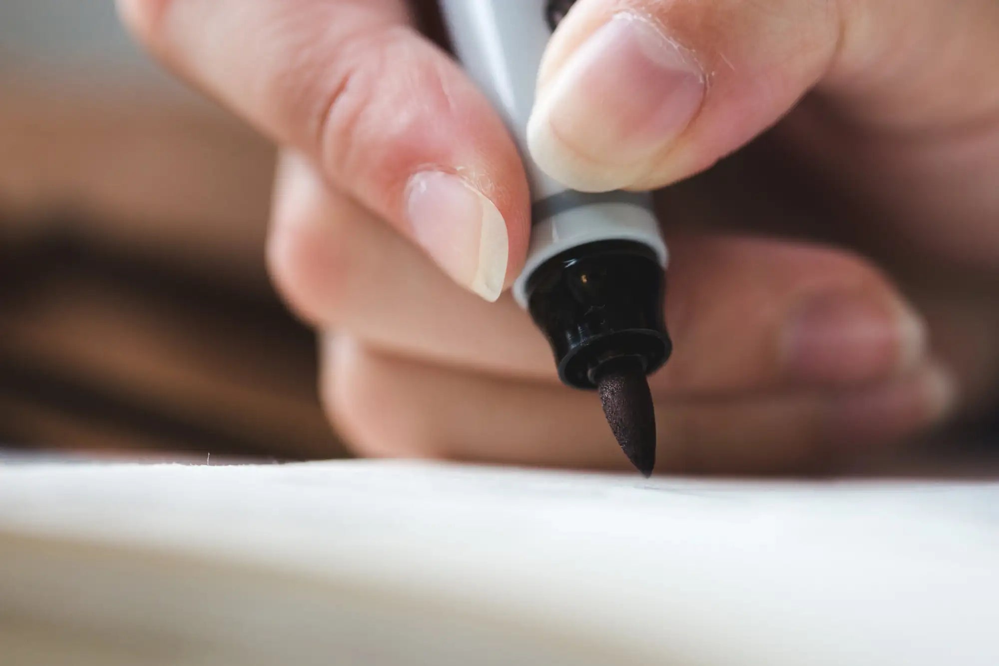 A sleek black marker with a silver barrel and fine tip, held steady by fingers poised above white paper.