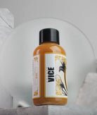 A sleek amber vice colors bottle with a black cap and floral label from the vice dijon daniels bauti set