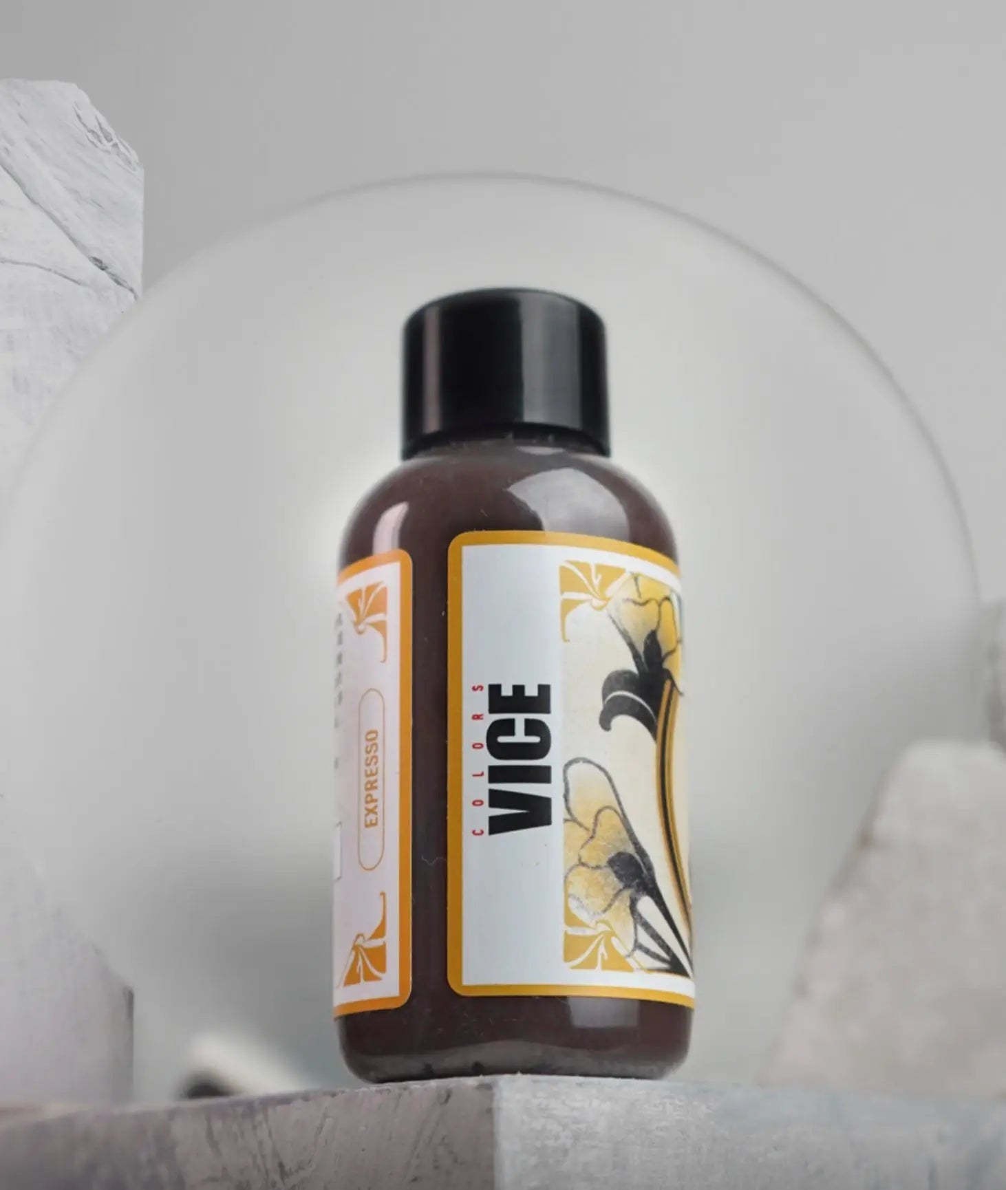 A sleek dark brown glass bottle with a black cap and yellow floral label for vice expresso daniels bauti set