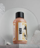 A sleek peach-colored vice extra light flesh liquid makeup bottle with a black cap and floral label from daniels bauti set