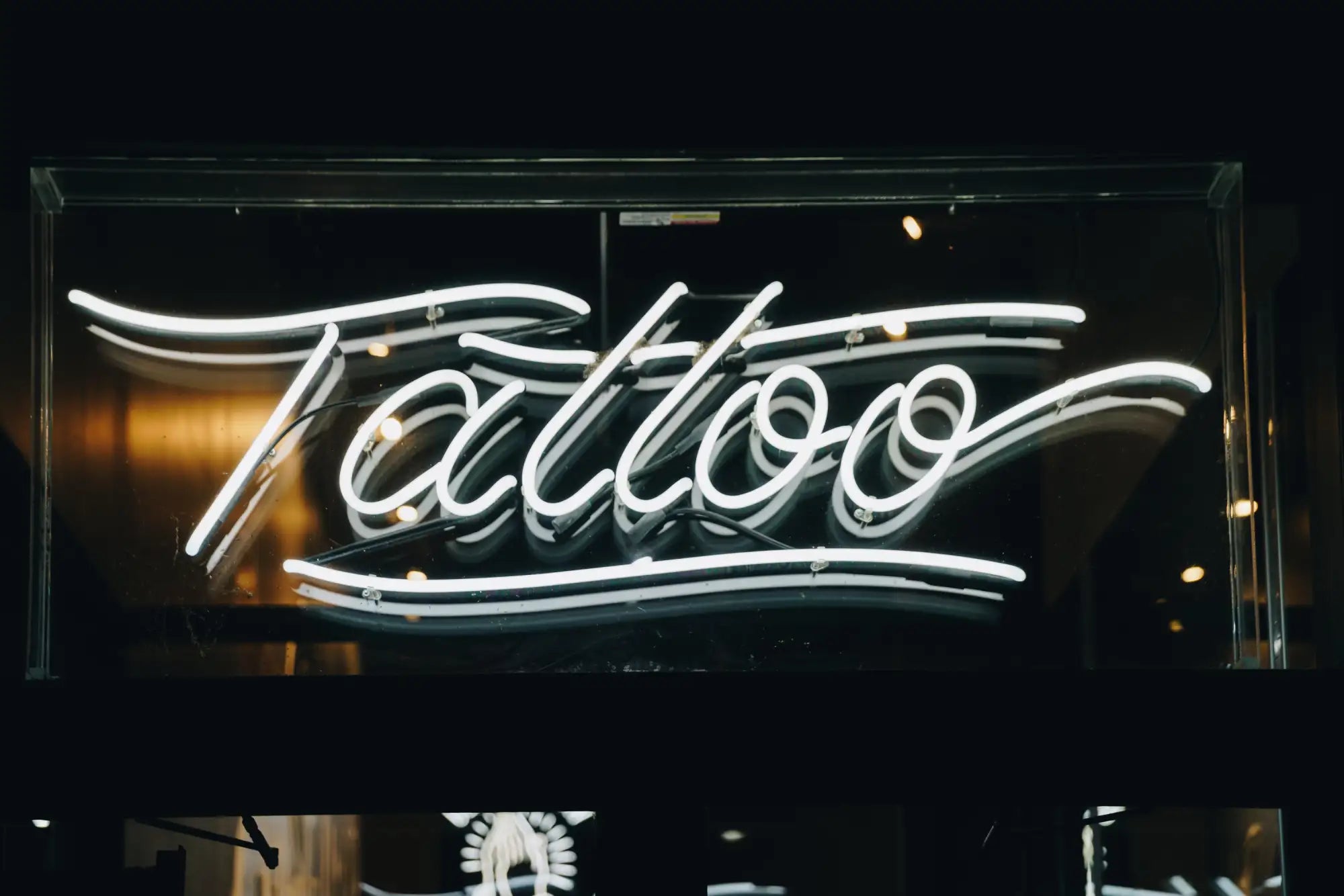 A glowing white neon sign with the word ’tattoo’ in elegant cursive script.